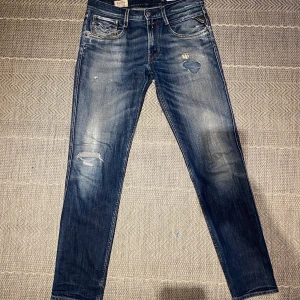 Blå jeans från Replay - Snygga blå jeans från Replay med slitna detaljer och en cool dragkedja på bakfickan. Perfekta för en avslappnad stil. Skick: 9/10. Pris kan diskuteras vid snabb affär.