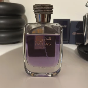 Lila parfym för män - Elegant parfymflaska med lila vätska och en stilren design. Flaskan har en fyrkantig form med rundade hörn och en dekorativ kork. Texten 'For Him' syns på framsidan, vilket indikerar att den är avsedd för herrar. Perfekt för den som söker en sofistikerad doft.