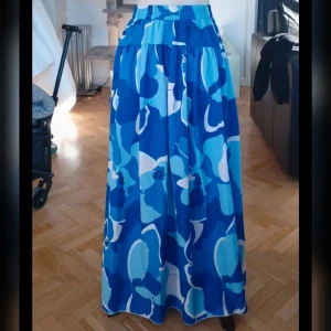 Blå blommig långkjol från Shein - Säljer en färgglad blå långkjol från Shein med ett stort blommönster i olika nyanser av blått och vitt. Kjolen har en elastisk midja för extra komfort. Perfekt för en somrig look!