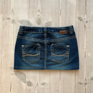 Lågmidjad jeanskjol  - Mörkblå lågmidjad jeanskjol från Tom Tailor som jag har sytt upp från en längre kjol. Storlek 36. Tvärs över midjan är det ca 39 cm och längs med sidan är det 31 cm. Fint skick. Använd gärna köp nu!.
