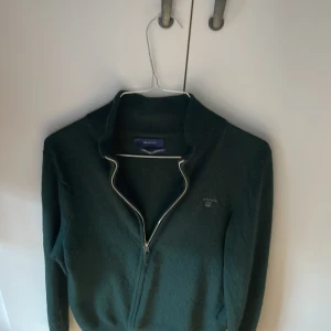Snygg mörkgrön Fullzip Gant Lambswool - Säljer en stilren mörkgrön fullzip från GANT i extra fin lammull. Det är en väldigt snygg grön nyans på tröjan. Den har långa ärmar och en diskret logga på bröstet. Passar både till vardags och mer uppklädda tillfällen. Hör gärna av er vid frågor eller funderingar! Och kolla gärna in mina andra annonser. Mvh Melker