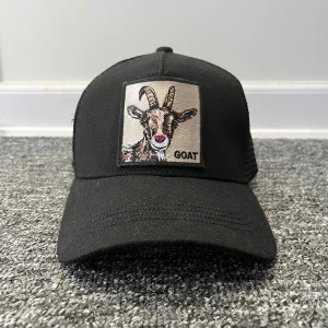 Goat keps  - Snygg svart keps med ett broderat getmotiv på framsidan. Kepsen har en klassisk design med nätpaneler på baksidan för extra ventilation. Perfekt för en avslappnad stil.