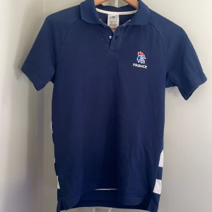 Mörkblå pikétröja från Adidas - Säljer en snygg mörkblå pikétröja från Adidas med korta vita ränder. Perfekt för en sportig stil.