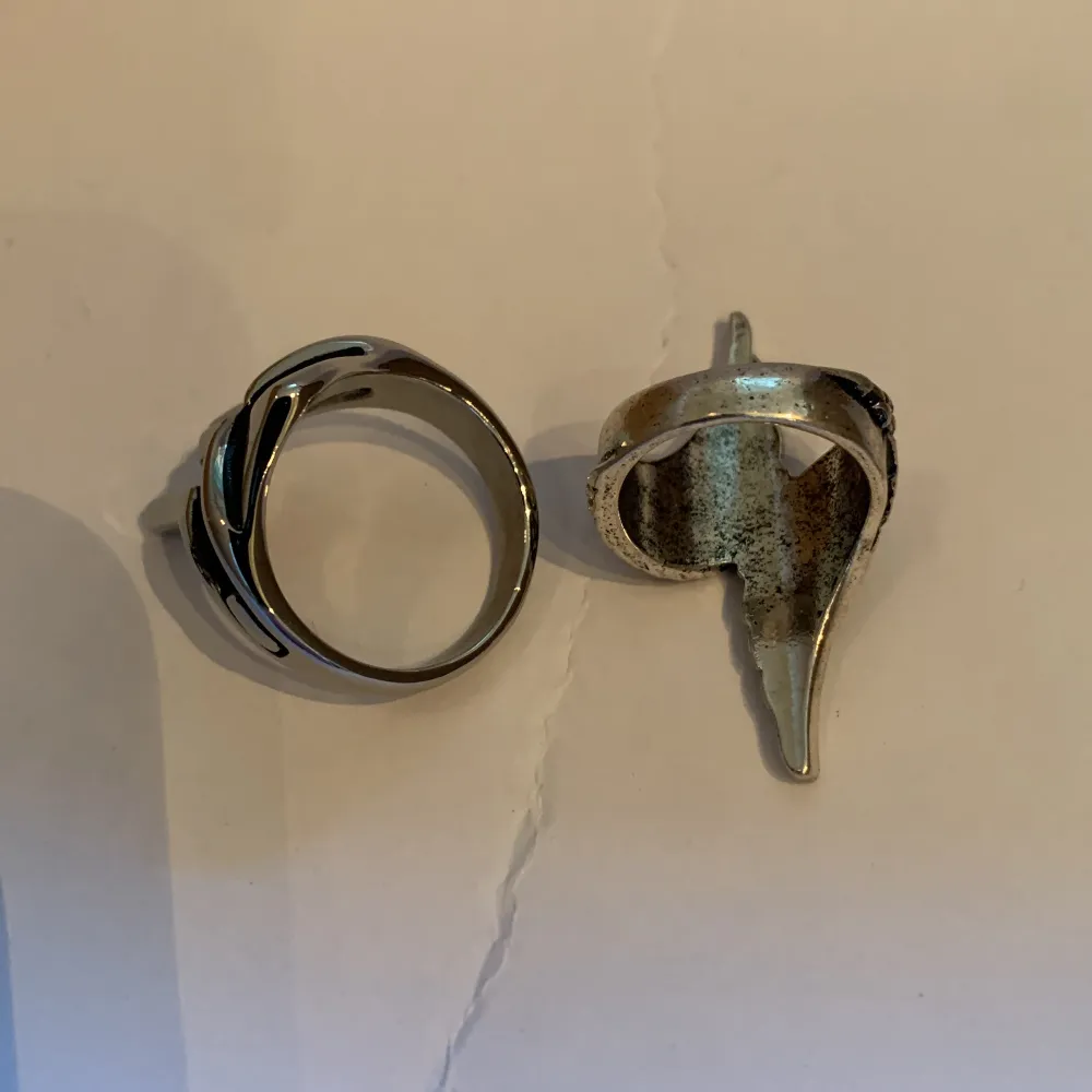 Två coola silverringar, en med en maskdesign och den andra med en vingdesign. Perfekta för att ge din stil en unik touch.. Asusteet.
