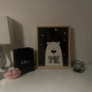 SMILE - En gullig tavla med en söt liten isbjörn på en mörk bakgrund med stjärnor runtom. Texten ‘SMILE’ står i 3D och lyser upp tavlan. Perfekt till barnrummet för att skapa en mysig och glad känsla.