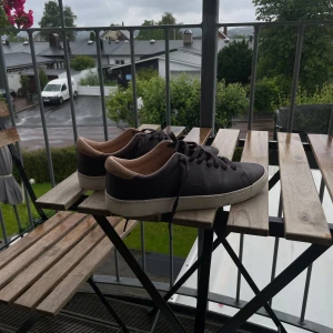 Bruna Fred Perry sneakers i skinn - Snygga bruna sneakers från Fred Perry i äkta skinn med beige insida och vit sula. Klassisk låg modell och diskret Fred Perry-logga på sidan. Skorna har svarta snören och stilren design som passar till det mesta. Skon har storlek 42. Skon har inga skador