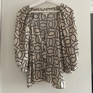 Blus HM - Söt somrig blus med djup v-ringning. Puffärmar med knäppning. Beige botten med svarta prickar. 