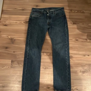 Levi's 501 jeans blå W31 L32 - Klassiska Levi's 501 jeans i blå denim med raka ben och knappgylf. Snygg vintagekänsla med tydliga sömmar och ikonisk läderpatch bak. Perfekta för dig som gillar tidlös stil. Jeansen är i bra skick. Om du vill ha mer bilder eller detaljer är det bara att höra av sig.