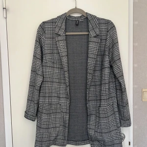 Rutig kavaj från H&M Divided, S - Snygg rutig kavaj från H&M Divided i svart, grått och vitt. Klassisk modell med krage, långa ärmar och två fickor framtill. Perfekt för dig som gillar en stilren och trendig look. Tunnare material som funkar året runt. Endast använd en gång.