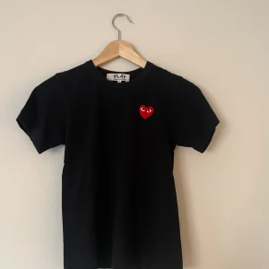 Svart Comme des Garçons Play t-shirt - Svart t-shirt från Comme des Garçons Play med det ikoniska röda hjärtat med ögon broderat på bröstet. Klassisk rund hals och korta ärmar. Tillverkad i mjuk bomull som är skön att bära hela dagen.