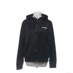 Svart hoodie från McKenzie XS - Svart hoodie från McKenzie i storlek XS. Klassisk modell med dragkedja framtill, snörning i huvan och fickor på magen. Perfekt för chill dagar eller när du vill ha en enkel och stilren look. Mjukt material och diskret logga på bröstet.