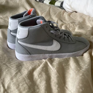 Grå Nike SB sneakers high-top - Snygga grå Nike SB high-top sneakers med vit sula och vit swoosh. Skorna har snörning, meshfoder och detaljer i vitt på hälen där det står NIKE. Aldrig använda ute. Strl 42