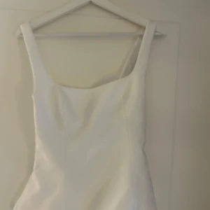 Vit kort klänning från Zara med knyt - Supersnygg vit kort topp från Zara med breda axelband och fyrkantig urringning. Baksidan har en öppen detalj med knytband som ger en trendig look. Perfekt för sommarens alla tillfällen och lätt att styla med accessoarer.