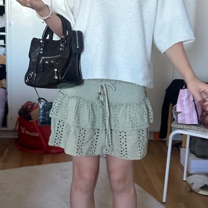 Beige volangkjol från Zara XS - Supersöt beige kortkjol från Zara med broderade hålmönster och dubbla volanger. Kjolen har smock i midjan och snörning med små tofsar. Perfekt för en chill och trendig look under varma dagar.