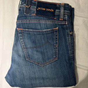 Jacob Cohën, storlek 33 - Snygga blå jeans från Jacob Cohën med orange kontrastsömmar. Jeansen är slim fit och i mycket bra skick. Nypris ligger på 3500, säljer nu för endast 999.