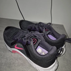 Svarta Nike sneakers med rosa detaljer - Jag säljer ett par träningsskor i mycket fint skick. Endast använda ett fåtal gånger inomhus.