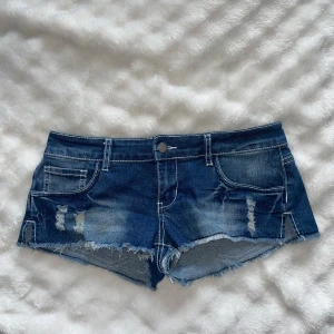 Blå slitna jeansshorts med fransig kant - Snygga blå jeansshorts med låg midja och slitna detaljer framtill. Shortsen har fransig kant nertill och klassiska fickor både fram och bak. Köpte på en second han affär i mos. Nypris för 1200kr. 