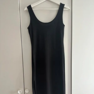 Svart klänning - En stilren svart klänning med rundad urringning. Klänningen har en rak passform och är tillverkad i ett mjukt, lätt glansigt material som ger en elegant look