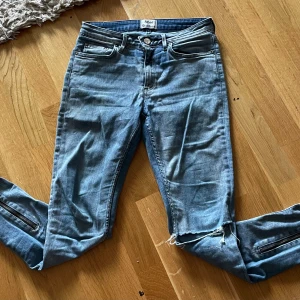 Acne Studios ljusblå skinny jeans 28/32 - Snygga ljusblå skinny jeans från Acne Studios med dragkedjor vid bensluten och råa kanter. Klassisk femficksmodell i stretchig denim som sitter tight hela vägen. Perfekta för dig som gillar en modern och edgy look.