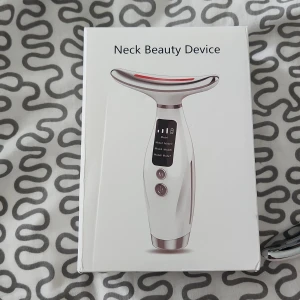Neck Beauty Device LED massager - Elektrisk Neck Beauty Device med LED-ljus i 7 färger och i 3 hastihet  Vit och silverfärgad, ergonomisk form med digital display och två knappar. Perfekt för ansikts- och halsvård, hjälper till att boosta hudens lyster och spänst. Laddningsbar och enkel att använda.