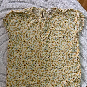 Blommig blus från Holly & Whyte - Supersöt blommig blus från Holly & Whyte by Lindex i storlek S. Topp i ljusgul nyans med små gula och gröna blommor, rund halsringning och knapp i nacken. Luftigt material, perfekt för varma dagar och en fräsch look. Ostruken på bilden men jag stryker den innan jag skickar.