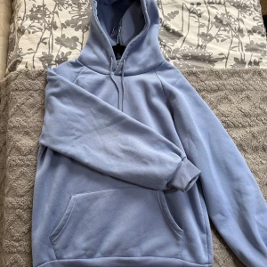 Ljusblå hoodie i storlek L - Enkel och stilren ljusblå hoodie med huva och snörning. Tröjan har en stor magficka och är tillverkad i mjukt material, perfekt för chill dagar. Långärmad och loose fit.