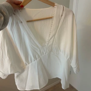 Vit blus med v-ringning och spetsdetaljer - Superfin vit blus med djup v-ringning och spetsdetaljer längs halsringningen. Blusen har trekvartsärmar och en luftig, lite lös passform. Aldrig använd!!