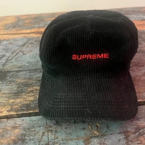 Svart manchesterkeps från Supreme - Supreme keps i svart manchester med röd broderad logga framtill. Klassisk böjd skärm och cool streetwear-vibe. Perfekt accessoar för dig som gillar stilrena detaljer och vill sticka ut med ett ikoniskt märke.