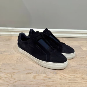 Axel Arigato 360 laceless - Stilrena mörkblåa sneakers från Axel Arigato i mocka med vit platt sula. Skorna har elastisk panel framtill istället för snörning och diskret logga på sidan. Perfekta för dig som gillar minimalistisk och clean design. Storlek 46