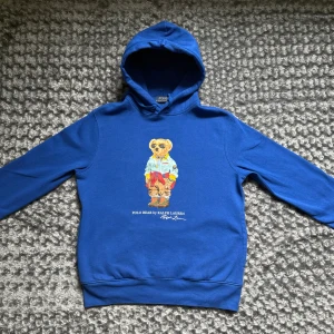 Blå hoodie Polo Ralph Lauren  - Blå Ralph Lauren hoodie, storlek S. Har ett tryck på framsidan och en liten fläck på ryggen, men inget som stör direkt. Skön att ha på sig och fortfarande helt okej skick.