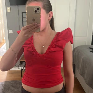 Röd volangtopp med djup v-ringning - Säljer en super fin röd topp med volangdetaljer på axlarna och djup v-ringning både fram och bak. Den ör även lite croppad! Den är aldrig använd men ingen prislapp kvar.🌸💕