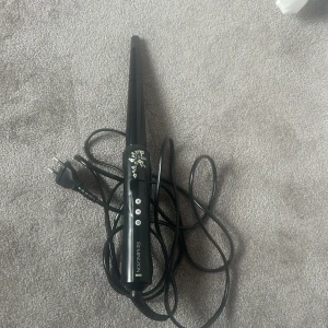 Remington locktång svart - Svart locktång från Remington med smal konformad stav och dekorativa silvriga detaljer. Utrustad med digital display och knappar för temperaturinställning. Perfekt för att skapa snygga lockar och vågor.