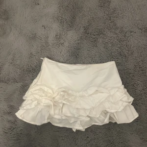 Vit volangkjol från Zara - Supersöt vit kortkjol från Zara med flera lager volanger som ger en lekfull och trendig look. Kjolen är i lätt material och har en feminin siluett, perfekt för dig som gillar en fräsch och stilren vibe.