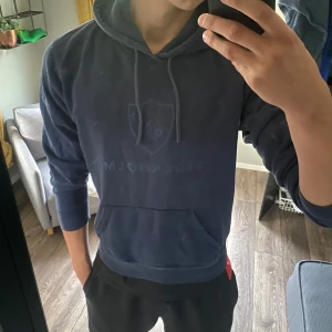 Blå DIF hoodie - Säljer en blå hoodie från Djurgårdens IF med stort DIF-emblem och texten Stockholm på bröstet. Tröjan har huva med snörning och en klassisk känguruficka framtill. Perfekt för dig som vill visa ditt stöd för laget och hålla stilen.