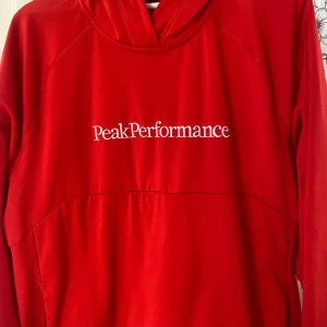 Röd hoodie Peak Performance XL - Riktigt snygg röd hoodie från Peak Performance i storlek XL. Tröjan har klassisk huva och stor vit logga broderad på bröstet. Perfekt för dig som gillar sportig och avslappnad stil. Materialet känns mjukt och följsamt mot kroppen.