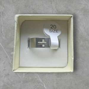 Bred silverring med korsmotiv - Cool bred ring i silverfärgad metall med ett utskuret kors mitt på. Ringen har en modern, minimalistisk design och passar perfekt för dig som gillar stilrena accessoarer med en twist. Storlek 20.2 mm (Rostfritt Stål)
