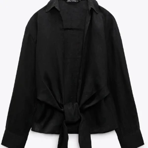Svart linneskjorta med knyt från Zara - Svart skjorta i linne från Zara med långa ärmar och snygg knytning framtill. Skjortan har klassisk krage och en lite croppad passform som ger en trendig vibe. Perfekt att styla med jeans eller kjol för en cool look.
