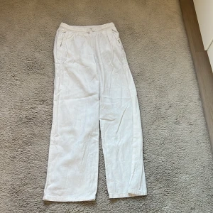 Vita linnebyxor med resårmidja - Säljer ett par vita linnebyxor med avslappnad passform och resår i midjan. Byxorna har raka ben och sidfickor, perfekta för en chill och luftig stil. Materialet är lätt och svalt, vilket gör dem grymma för varmare dagar.