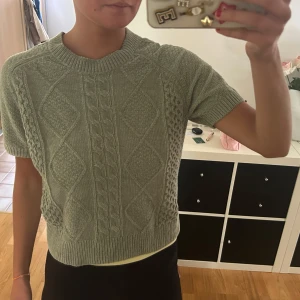 Stickad grå tröja från KappAhl XS - Supersöt stickad tröja från KappAhl i ljusgrått med korta ärmar och kabelstickat mönster framtill. 