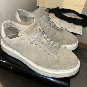 Grå mockasneakers från Legend - Snygga sneakers från Legend i ljusgrå mocka med matchande grå skosnören och vit, platt sula. Klassisk och stilren design med rund tå och diskret branding på plösen. Perfekta för dig som gillar minimalistisk stil.
