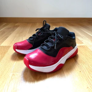 Nike Jordan 11 Low i mycket fint skick - Snygga Nike Jordan 11 Low sneakers i svart och rött med vit sula. Skorna har glansig röd tå och sidor, svart mesh och skinn upptill samt klassisk Jumpman-logga på innersulan. Sparsamt använda, mycket fint skick. 