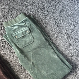 Gröna mjukisbyxor i sammet från Juciy Couture  - Mörkgröna mjukisbyxor i mjuk sammet med bred resår i midjan och en ficka med knappar bak. Perfekta för chill dagar eller när du vill vara extra bekväm.