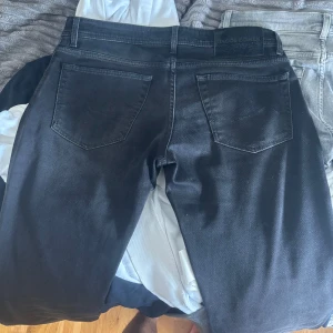 Svarta jeans från Jacob Cohën, stl 33 - Snygga svarta jeans från Jacob Cohën i klassisk femficksmodell. Jeansen är tillverkade i Italien och har diskreta detaljer samt svart patch med logga bak. Materialet är mjukt och stretchigt för en bekväm passform.