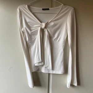 Vit långärmad topp med knyt från Missay - Säljer en vit långärmad topp från Missay med snygg knytning framtill och v-ringad hals. Toppen har en liten svart fläck(kolla bilderna) men jag är övertygad om att den går bort i tvätten!