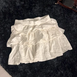 Vit volangkjol med bred midja - Supersöt vit kortkjol med flera lager volanger och bred midja. Kjolen har en luftig känsla och passar perfekt till sneakers eller sandaler. Materialet känns lätt och flowy, perfekt för varma dagar.