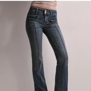 Blå jeans med fickdetaljer - Snygga blå jeans med raka ben och markerade sömmar framtill. Byxorna har dubbla knappar i midjan och coola fickor med lock framtill. Perfekt för dig som gillar en trendig och avslappnad stil.