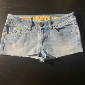 Ljusblå jeansshorts från Jacob Cohen - Snygga ljusblå jeansshorts från Jacob Cohen med rå kant nertill och klassiska fem fickor. Shortsen har detaljerade sömmar, knappgylf och en broderad logga på myntfickan. Perfekta för varma dagar när du vill ha en chill och trendig look.                                                                Size 28 men passar större🥰 Skriv för mer detaljer ✌️