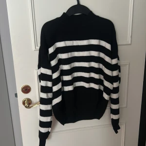 Svartvit randig stickad tröja - Säljer en svartvit stickad tröja med breda horisontella ränder. Tröjan har en högre hals och långa ärmar med ribbade muddar. Materialet är mjukt och skönt stickat, perfekt för kyliga dagar. Passformen är lite loose och ger en avslappnad vibe. Inga hål är sådant men den är använd 💕Den är från HM eller Lindex