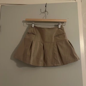 Beige pleated minikjol med fickor - Beige pleated minikjol med två framfickor i strl. Xs. Dragkedja därbakom och är i gott skick 
