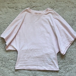 Ljusrosa t-shirt från Nelly - Säljer en ljusrosa topp från Nelly i storlek XXS. T-shirten har korta, breda ärmar och en loose passform som ger en chill vibe. Materialet är mjuk bomull och färgen är riktigt söt och fräsch. Perfekt för dig som gillar enkel och clean stil. Det är inte den toppen med en knytning i ryggen!! Jätte bra skick endast andvänd en gång. Ny pris ungefär 300